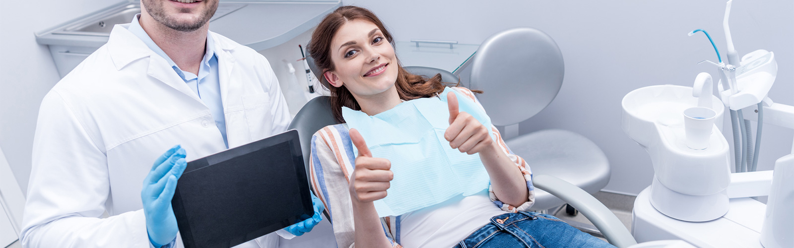 Happy patient showing thumbs-up in the dentist chair with the doctor